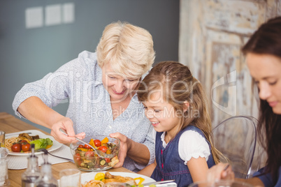 Grandmother serving granddaughter while having breakfast