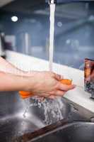 Woman cleaning carrots at kitchen washbasin