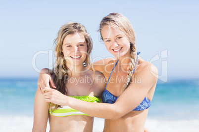 Portrait of two happy women in bikini standing on the beach