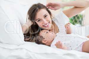 Smiling woman lying with baby on bed