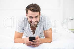 Portrait of happy man using mobile phone on bed