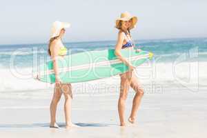 Two women carrying surfboard on the beach