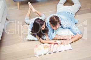 Father and daughter with picture book lying on floor