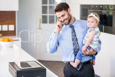 Businessman talking on mobile phone while carrying daughter