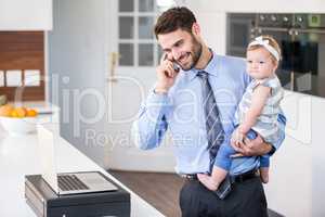 Businessman talking on mobile phone while carrying daughter