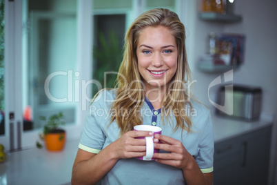 Young woman drinking coffee while standing in kitchen