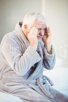 Senior man suffering from headache while sitting on bed