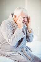 Senior man suffering from headache while sitting on bed