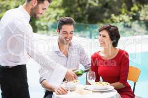Smiling waiter serving red wine to couple