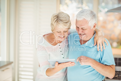 Happy senior couple holding digital tablet in kitchen