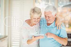 Happy senior couple holding digital tablet in kitchen