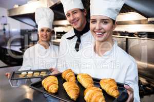 Three chefs holding a tray of baked croissant and cookies