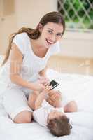 Smiling mother holding mobile phone while playing with baby