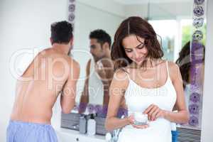 Woman holding cream while husband in background