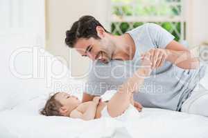 Smiling father playing with baby on bed