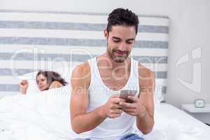 Man using mobile phone while wife sleeping in background