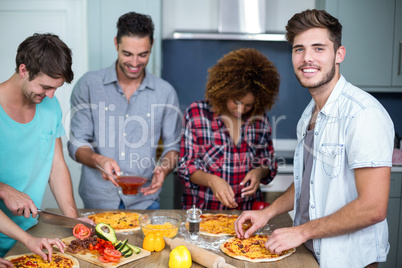 Young man preparing pizza with friends on table