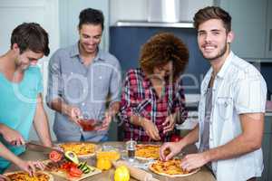 Young man preparing pizza with friends on table