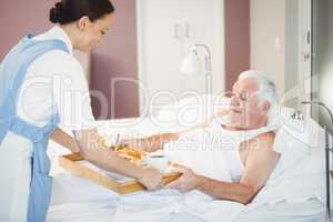 Nurse giving breakfast with senior man lying on bed