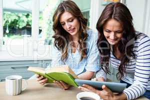 Female friends using digital tablet and reading book