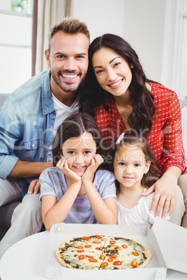 Family of four enjoying pizza while sitting on sofa