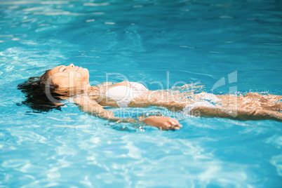 Beautiful woman in white bikini floating in swimming pool