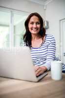 Portrait of cheerful woman working on laptop while holding coffe