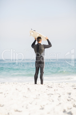 Rear view of man holding surfboard over head