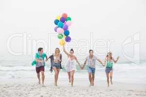Group of friends running on the beach with balloons