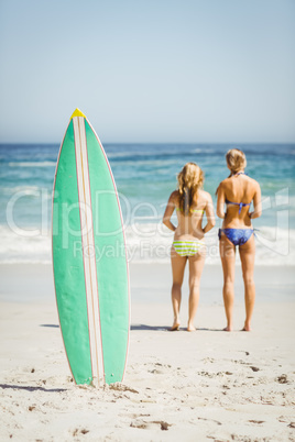 Surfboard in sand and rear view of two women looking at sea