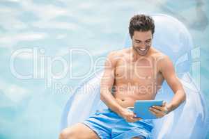 Shirtless man using digital tablet on swim ring