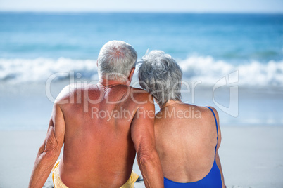 Cute mature couple sitting on the beach looking at the sea