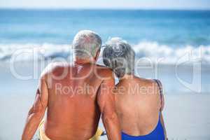 Cute mature couple sitting on the beach looking at the sea