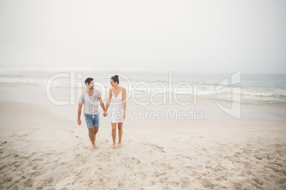 Happy couple holding hands and walking on the beach