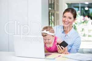 Woman holding mobile phone while sitting with baby girl