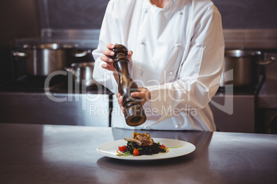 Chef sprinkling pepper on dish