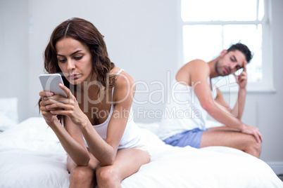 Woman using mobile phone while tensed husband in background
