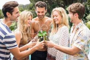 Group of friends toasting beer bottles near pool