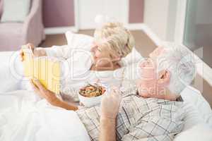 Couple reading book while having breakfast on bed