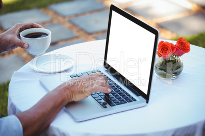 Close up of masculine hands using laptop and having coffee