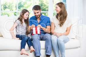 Man opening gift while sitting on sofa with family