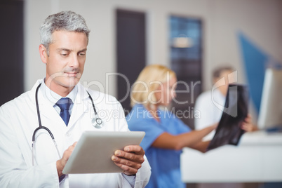 Male doctor using digital tablet with colleague checking X-ray