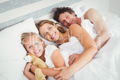 High angle view of smiling family relaxing on bed