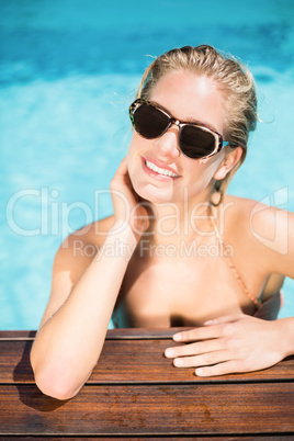 Beautiful woman wearing sunglasses leaning by poolside