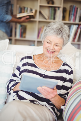 Happy senior woman using tablet while sitting on sofa