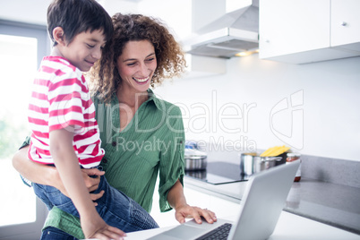 Mother and son using laptop in kitchen