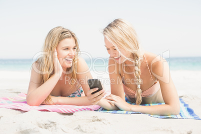 Two woman lying on the beach and looking at mobile phone