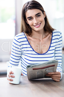 Happy young woman with newspaper and mug