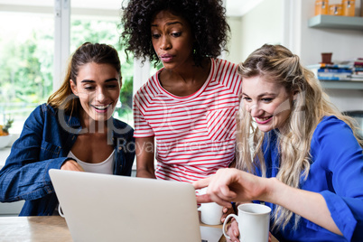 Female friends smiling while looking in laptop