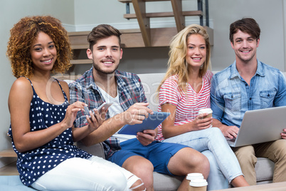 Friends smiling while using technologies on sofa